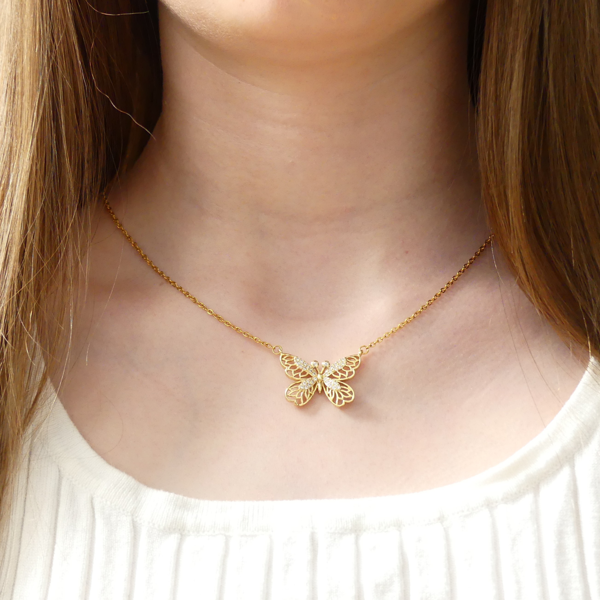 Gold crystal butterfly pendant necklace on a person wearing a white top